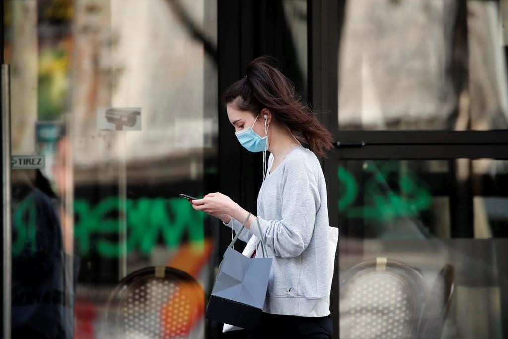 A woman wearing protective face mask walks looking at her phone past a closed restaurant during a nationwide confinement to counter the COVID-19, in Paris, Monday, April 20, 2020.
