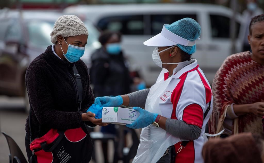 A health worker hands over surgical gloves to a woman, whilst queuing to undergo screening and testing for COVID-19, in Lenasia, south of Johannesburg, South Africa, Wednesday, April 8, 2020. South Africa and more than half of Africa's 54 countries have imposed lockdowns, curfews, travel bans or other restrictions to try to contain the spread of COVID-19. The new coronavirus causes mild or moderate symptoms for most people, but for some, especially older adults and people with existing health problems, it can cause more severe illness or death. (AP Photo/Themba Hadebe).