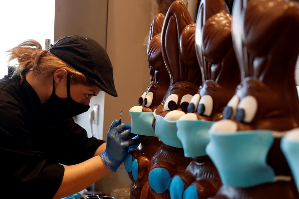 An employee of cake shop prepares chocolate Easter bunnies with masks in Lykovrisi, northern Athens, on Wednesday, April 8, 2020.