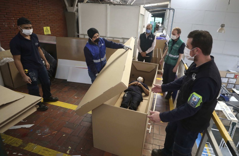 Rodolfo Gomez, to center, and his employees demonstrate how their design of a cardboard box can serve as both a hospital bed and a coffin, designed for COVID-19 patients, in Bogota, Colombia, Friday, May 8, 2020. Gomez said he plans to donate the first units to Colombia’s Amazonas state, and that he will sell others to small hospitals for 87 dollars.