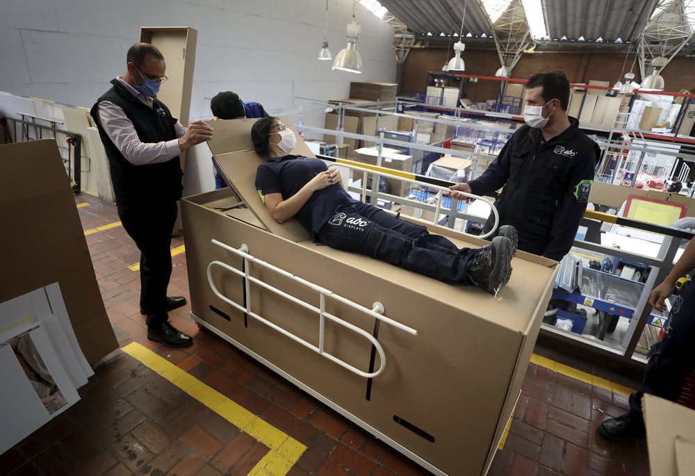 Rodolfo Gomez, left, and his employees demonstrate how their design of a cardboard box can serve as both a hospital bed and a coffin, designed for COVID-19 patients, in Bogota, Colombia, Friday, May 8, 2020. Gomez said he plans to donate the first units to Colombia's Amazonas state, and that he will sell others to small hospitals for 87 dollars. 