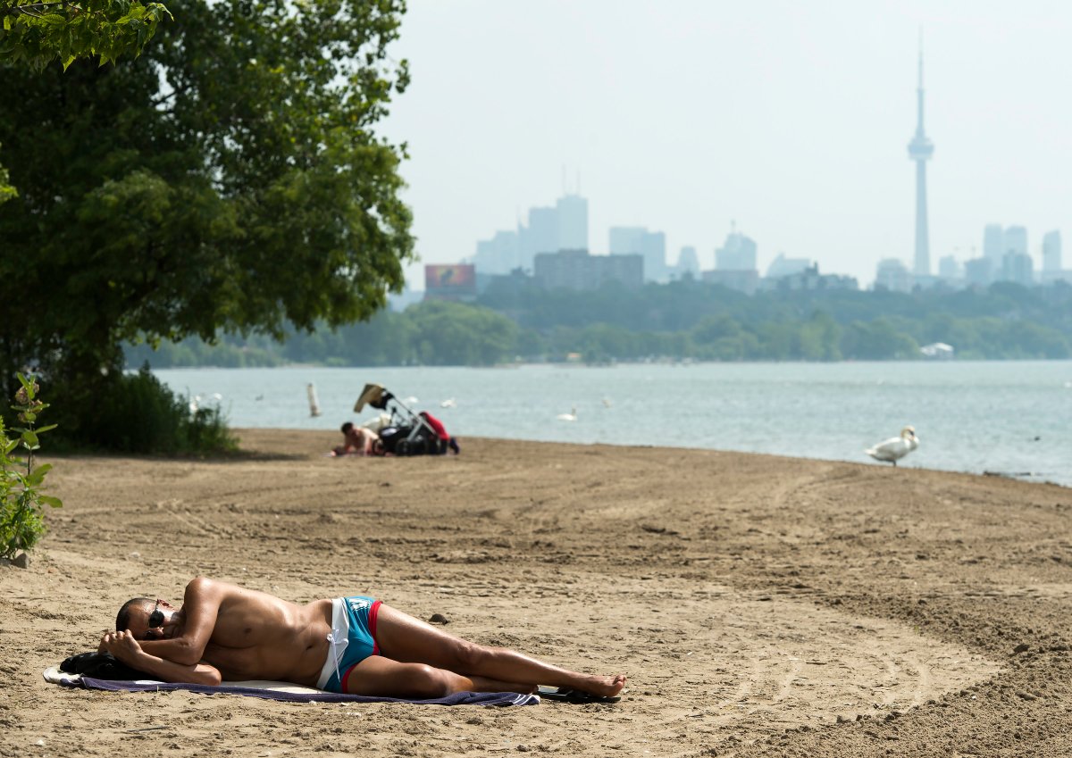 A man sleeps on the sandy beach along Lake Ontario in the extreme heat in Toronto on Friday, July 19, 2019. 