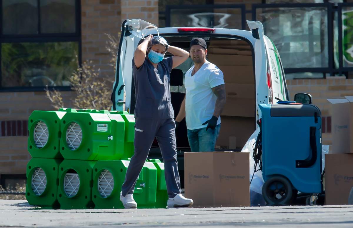 A front line worker adjusts her PPE as she walks past another worker unloading air filters and cleaning equipment at Orchard Villa care home in Pickering, Ont. on Monday April 27, 2020. 