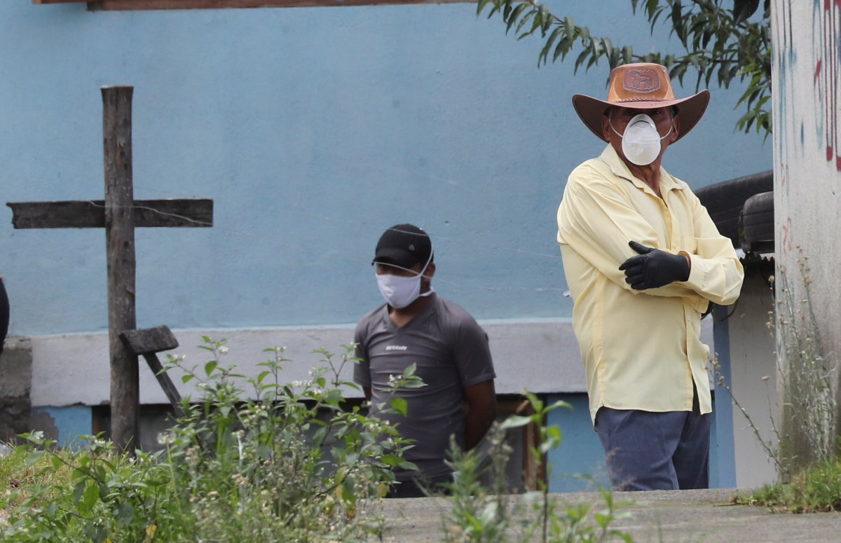 Residents, wearing protective face masks and gloves, watch as journalists arrive in their neighborhood to confirm the death of a neighbour who allegedly died of the new coronavirus, in San Juan de Conocoto, near Quito, Ecuador, Friday, May 1, 2020. 
