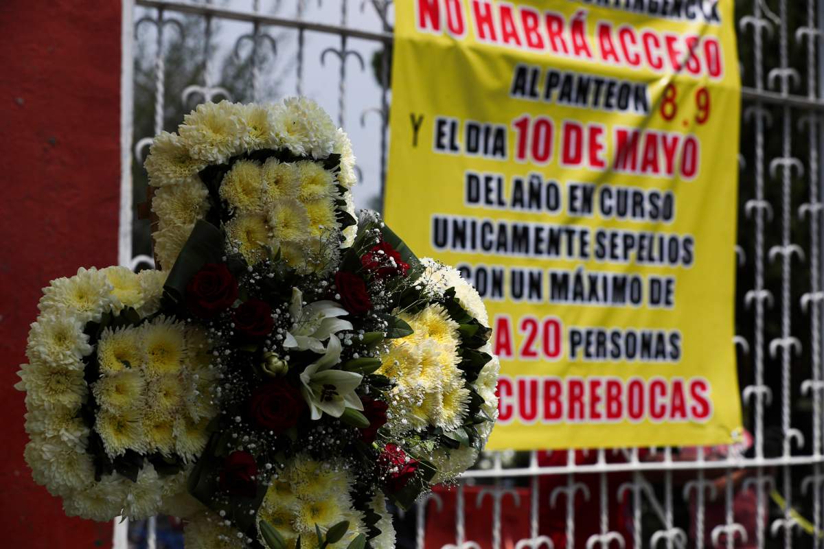 A funeral wreath is displayed at the entrance of the San Isidro cemetery near a sign that reads in Spanish: "There will be no access to the cemetery on May 8, 9 and 10" in Mexico City, Friday, May 8, 2020.