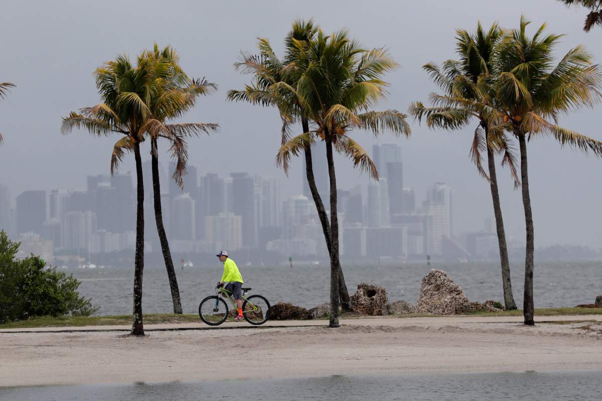 The Miami skyline is shrouded in clouds as a cyclist rides along Biscayne Bay at Matheson Hammock Park, Friday, May 15, 2020.