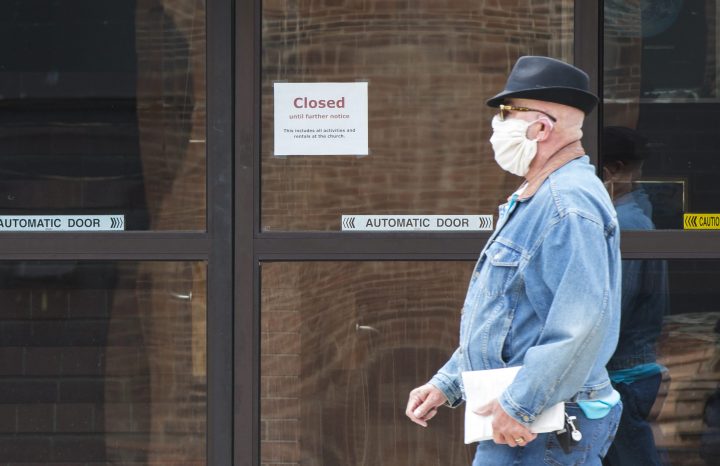 A man wearing a face mask walks past a closed church.
