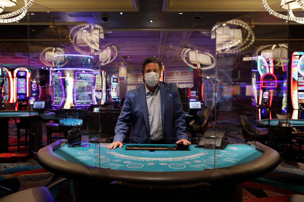 Bill Hornbuckle, acting CEO and president of MGM Resorts International, poses behind acrylic barriers used as a coronavirus safety precaution at a blackjack table in the closed Bellagio hotel and casino, Wednesday, May 20, 2020, in Las Vegas. Casino operators in Las Vegas are awaiting word when they will be able to reopen after a shutdown during the coronavirus outbreak.