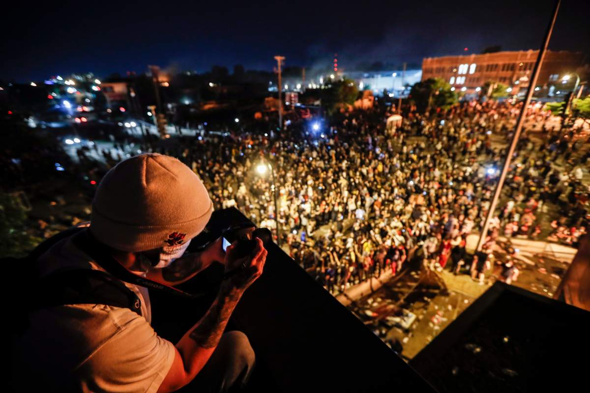 A protestor takes a picture of a demonstration from the roof of the Minneapolis 3rd Police Precinct, Thursday, May 28, 2020, in Minneapolis. (AP Photo/John Minchillo)