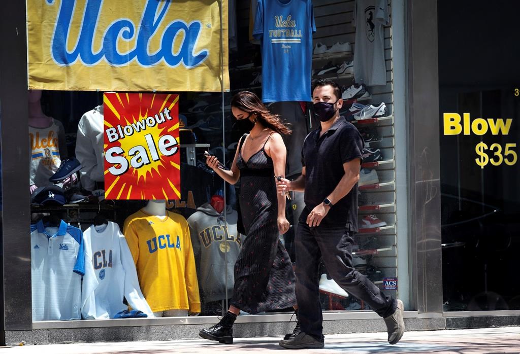 A couple wearing protective masks from the coronavirus walk down the street in the Westwood section of Los Angeles on Friday, May 15, 2020.