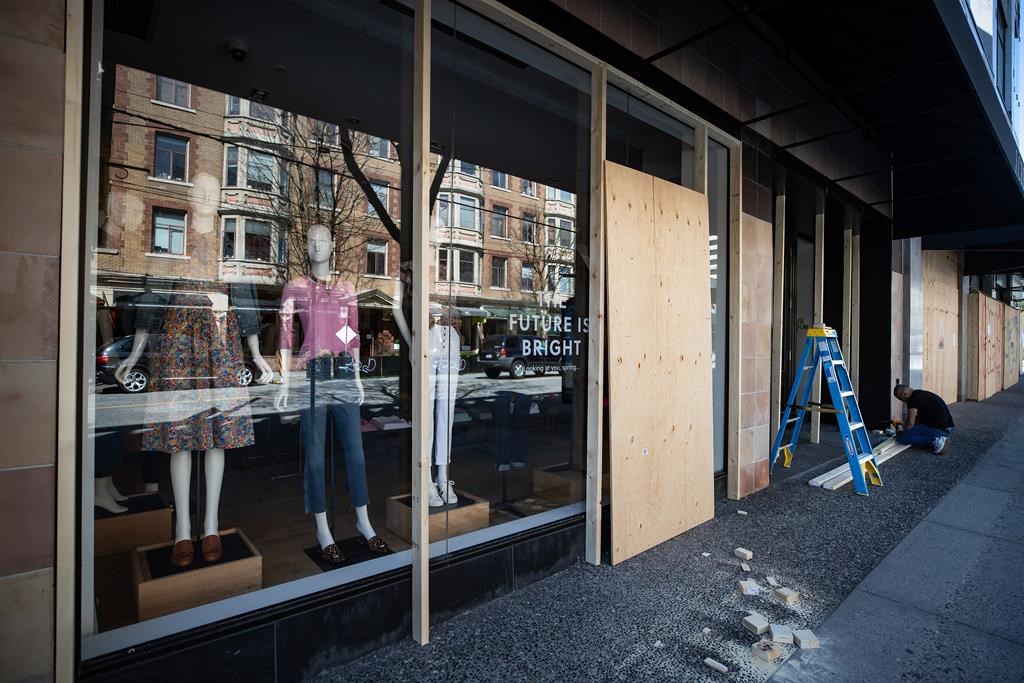 A worker boards up a closed clothing store in Vancouver, on Thursday, April 16, 2020.