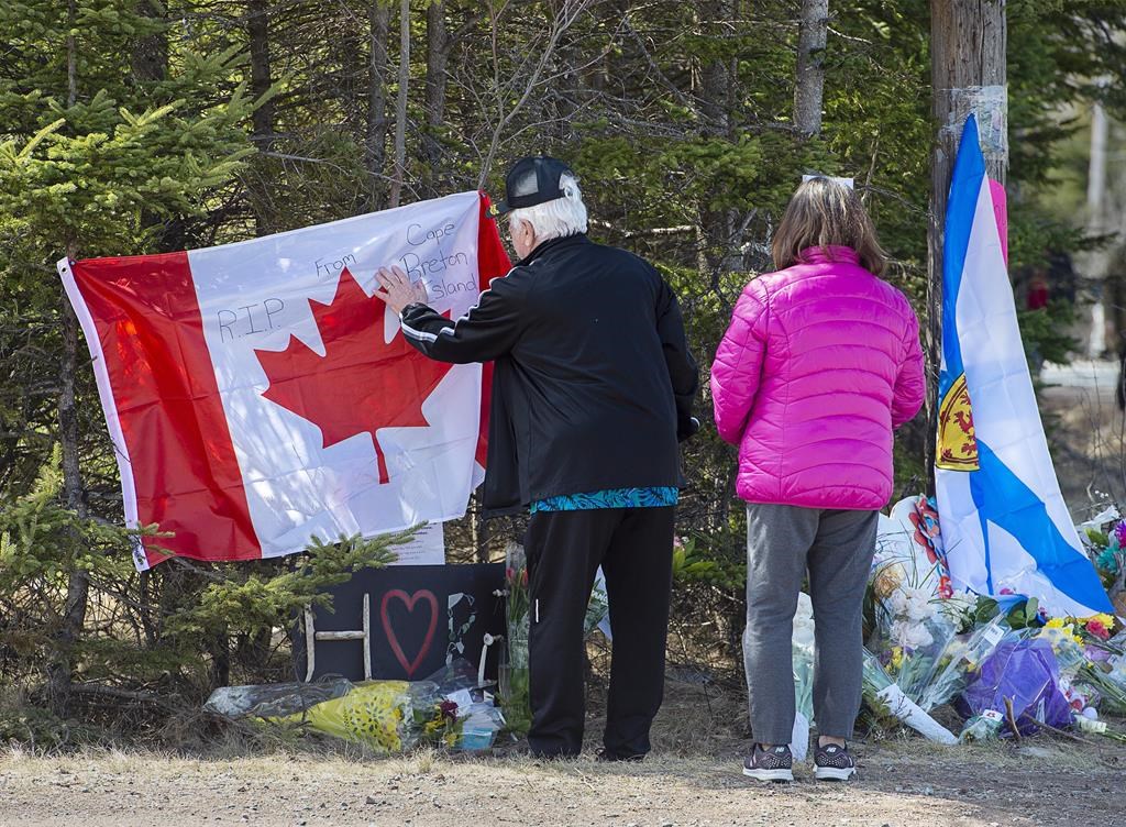 A couple place a flag at a memorial in Portapique, N.S. on Wednesday, April 22, 2021. THE CANADIAN PRESS/Andrew Vaughan