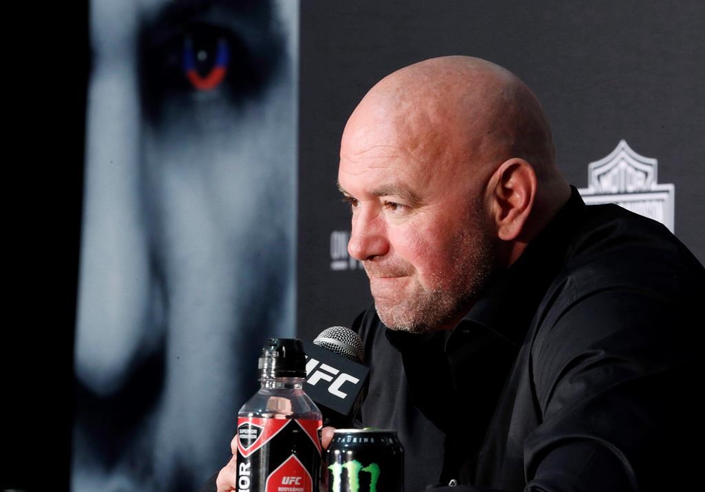 UFC boss Dana White leans into a microphone to speak at a press conference. He is wearing a black shirt.