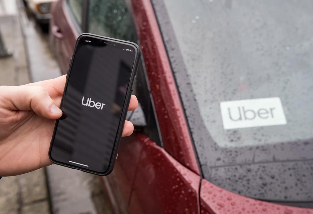 The Uber app is seen on an iPhone near a driver's vehicle.