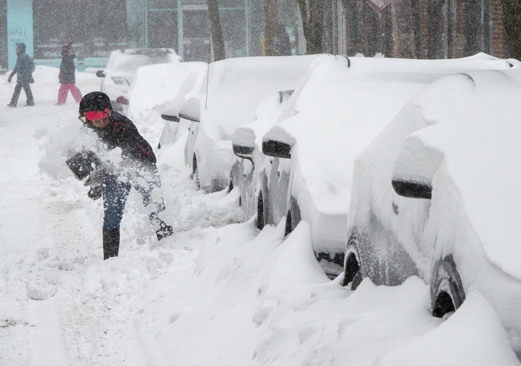 A woman shovels out her car during a snowstorm.