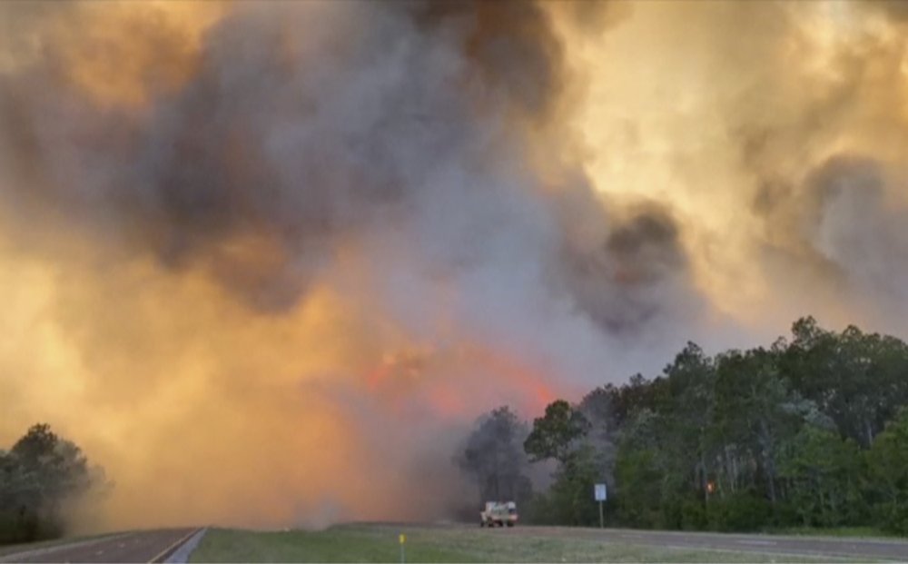 In this image made from video taken May 6, 2020 by the Florida Department of Agriculture and Consumer Services, fire and smoke rise from trees alongside a road in Santa Rosa County, Florida. Wildfires raging in the Florida Panhandle have forced nearly 500 people to evacuate from their homes, authorities said. (Florida Department of Agriculture and Consumer Services via AP)
.