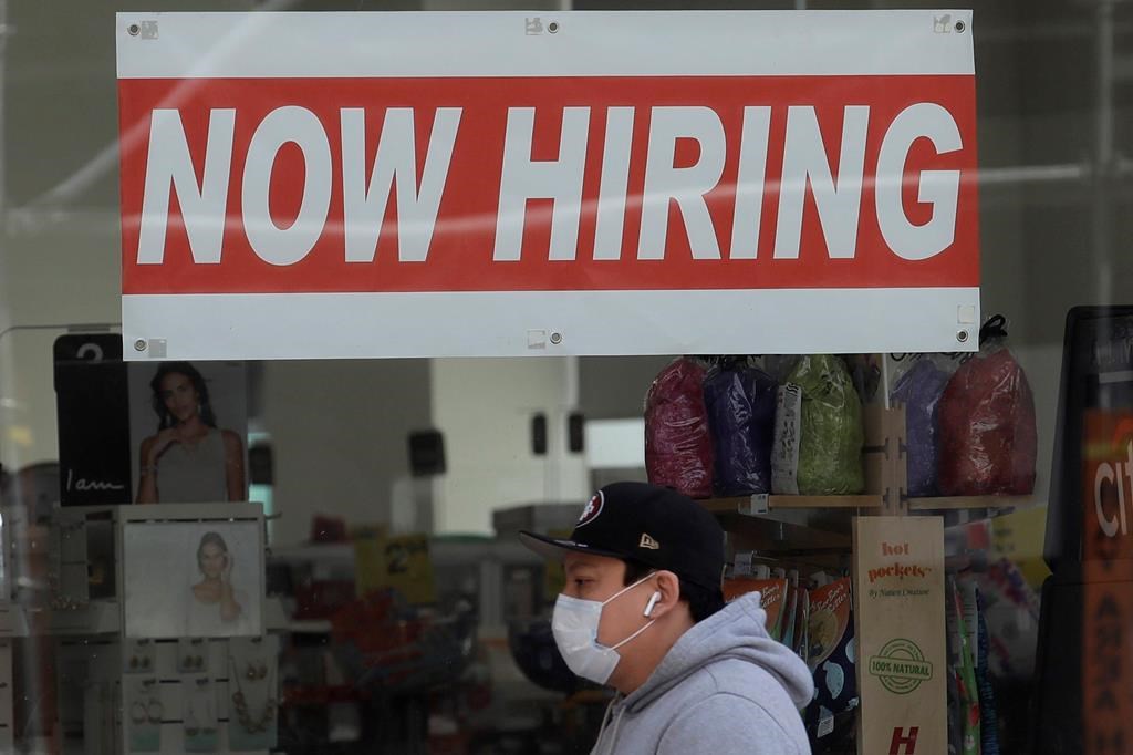 FILE - This May 7, 2020, file photo shows a man wearing a mask while walking under a Now Hiring sign at a CVS Pharmacy during the coronavirus outbreak in San Francisco. California's unemployment rate nearly tripled in April because of the economic fallout from coronavirus pandemic. (AP Photo/Jeff Chiu, File).