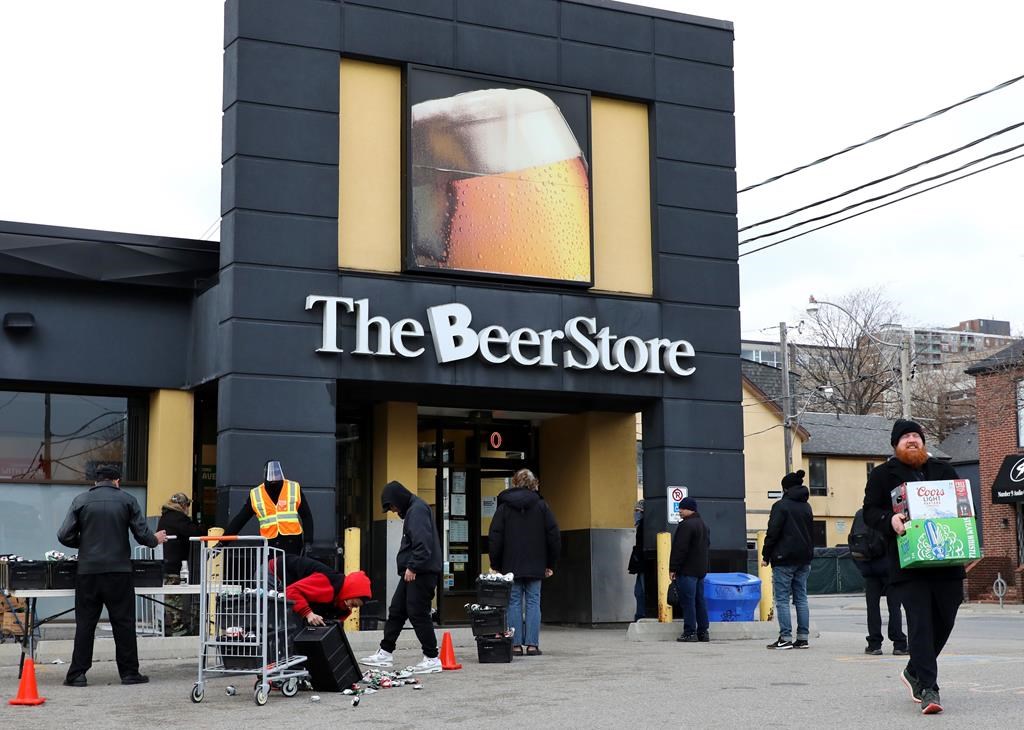 People line up in a parking lot for a long wait to return empties or buy beer at a Beer Store in downtown Toronto on April 16, 2020. A Toronto brewery is issuing a plea for consumers to bring back their empty bottles as the Beer Store says a growing number of its locations are accepting returns. Steam Whistle Brewery says restrictions related to the COVID-19 pandemic have led to a decline in bottle returns, leaving it with a potential shortage just as sales are expected to ramp up for spring and summer.