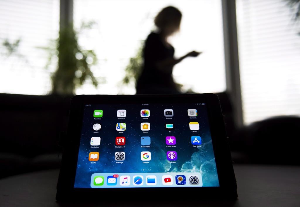 A woman uses her smartphone as apps are shown on an iPad in Mississauga, Ont., on Monday, Nov. 13, 2017.
