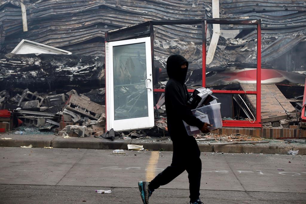 A man carries items past a burned out Auto Zone store near the Minneapolis Police Third Precinct Thursday, May 28, 2020, after a night of rioting and looting as protests continue over the death of George Floyd.