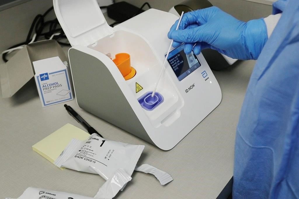 FILE - In this April 10, 2020, file image made from video, a lab technician dips a sample into the Abbott Laboratories ID Now testing machine at the Detroit Health Center in Detroit. Federal health officials are warning about potential accuracy problems with the rapid test for COVID-19 used at thousands of hospitals, clinics and testing sites across the U.S., including the White House.