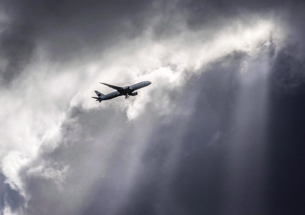 An Air Canada plane flies underneath dark clouds illuminated by some sun rays above Frankfurt, Germany, Thursday, March 2, 2017.