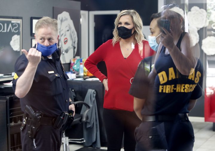 Salon owner Shelley Luther, centre, listens to Dallas City officials as a reflection of a supporter filming them is seen from outside Luther’s reopened Salon A la Mode in Dallas, Friday, April 24, 2020.