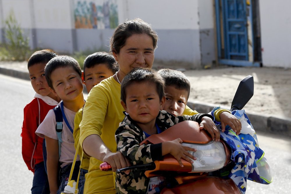 FILE – In this Sept. 20, 2018 file photo, a Uighur woman and children sit on a motor-tricycle after school at the Unity New Village in Hotan, in western China’s Xinjiang region. Birth rates in the mostly Uighur regions of Hotan and Kashgar have plunged by more than 60% since 2015, government statistics show.