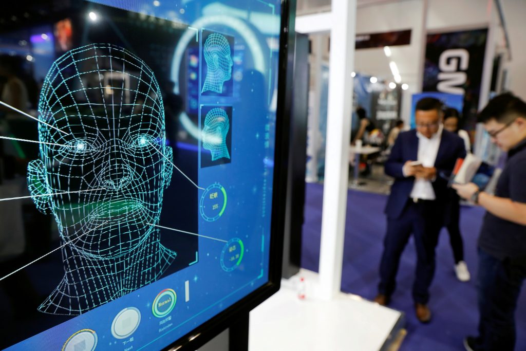 FILE PHOTO: Visitors check their phones behind the screen advertising facial recognition software during Global Mobile Internet Conference (GMIC) at the National Convention in Beijing, China April 27, 2018. 