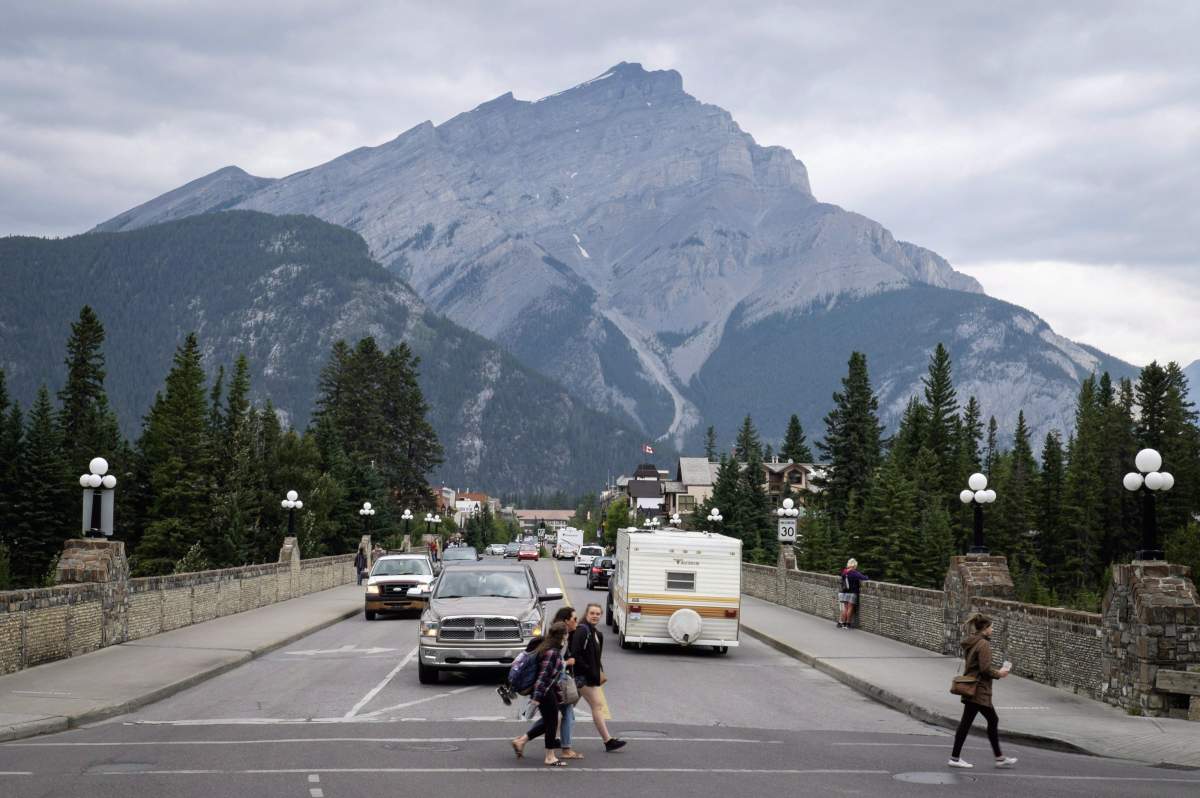 People walk across a street in the town of Banff in Banff National Park on Friday, July 21, 2017.