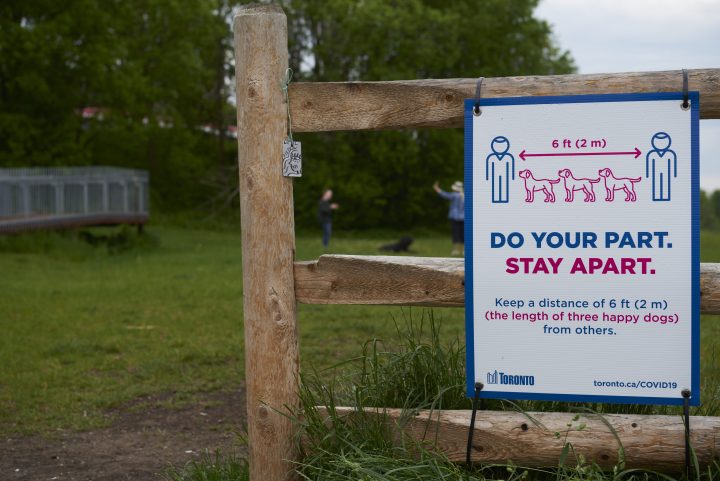 A sign reminds people to stay six feet apart -- or the length of three happy dogs -- at an off leash dog park in Toronto, Ont., on May 29, 2020, during the COVID-19 pandemic.