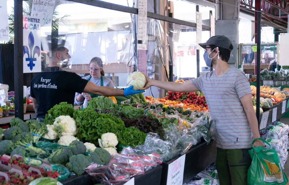 A client shops through a plexiglass shield at Montreal's Jean Talon Market, on Tuesday, June 16, 2020. 