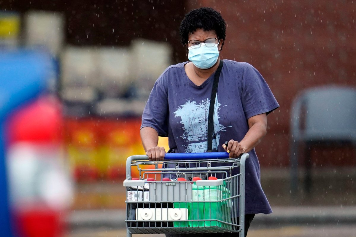 A shopper wears a mask as she pushes her grocery cart in the rain Thursday, June 25, 2020, in Houston. Texas Gov. Greg Abbott said Wednesday that the state is facing a "massive outbreak" in the coronavirus pandemic and that some new local restrictions may be needed to protect hospital space for new patients.