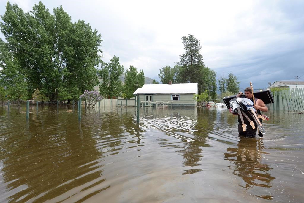 Resident Lars Androsoff carries his friend’s guitars as he walks through the floodwaters in Grand Forks, B.C., on Thursday, May 17, 2018. The Canadian Press