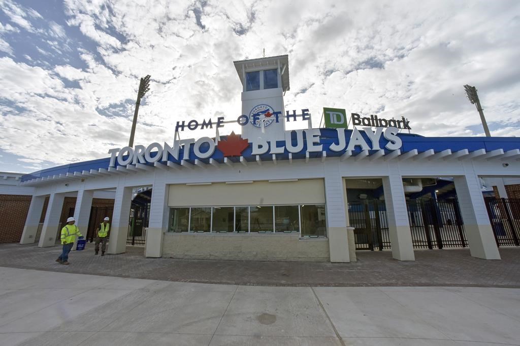 Several players and staff members on the Toronto Blue Jays have tested positive for COVID-19, a source has told The Canadian Press. Construction workers walk past the main entrance to the TD Ballpark, the Florida home of Toronto Blue Jays, as they get the stadium ready in Dunedin, Fla., Sunday, Feb. 16, 2020. THE CANADIAN PRESS/Steve Nesius.