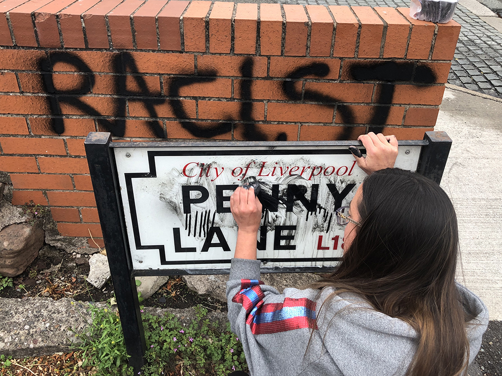 Local resident Lucy Comerford cleans a road sign for Penny Lane, made famous by The Beatles, in Liverpool, England, after it was vandalized following perceived links with slave trader James Penny.