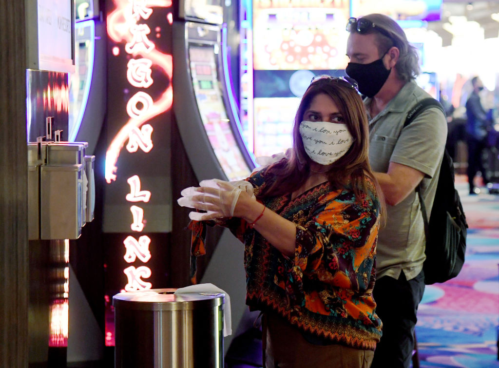Guests take complimentary gloves from the side of a new hand-washing station on the gaming floor that also offers masks and wipes at Bellagio Resort & Casino on the Las Vegas Strip.
