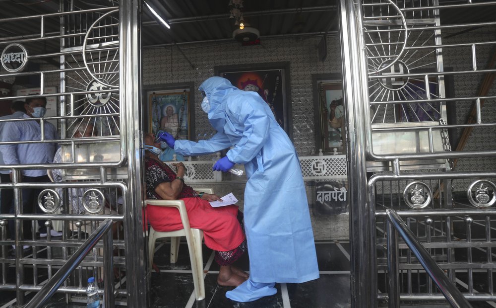 A health worker takes a swab test of a women at a temple in Mumbai, India, Saturday, July 18, 2020. India crossed 1 million coronavirus cases on Friday, third only to the United States and Brazil, prompting concerns about its readiness to confront an inevitable surge that could overwhelm hospitals and test the country's feeble health care system.