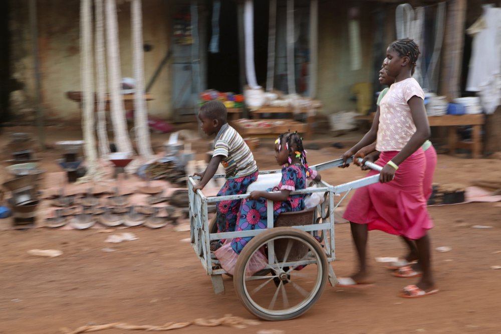 Girls push children in a cart near the market in the town of Hounde, Tuy Province, in southwestern Burkina Faso on Thursday, June 11, 2020.