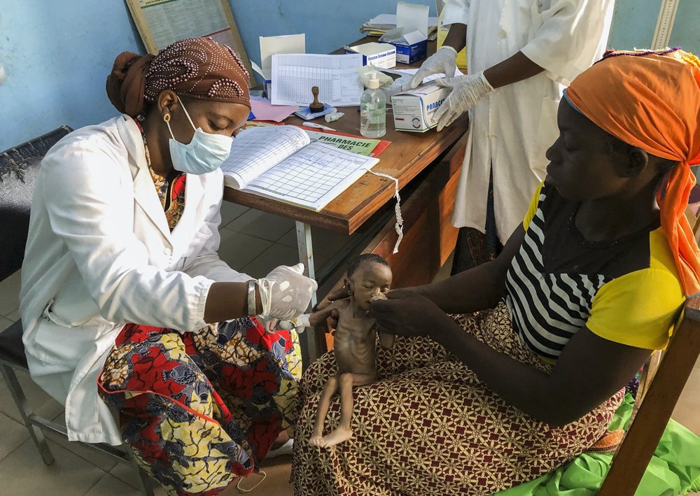 One-month old Haboue Solange Boue sits on the lap of her mother Danssanin Lanizou, 30, right, as a nurse inserts an intravenous drip into her arm to treat her for severe malnutrition at the feeding center of the main hospital in the town of Hounde, Tuy Province, in southwestern Burkina Faso on Thursday, June 11, 2020. All around the world, the coronavirus and its restrictions are pushing already hungry communities over the edge, cutting off meager farms from markets and isolating villages from food and medical aid.