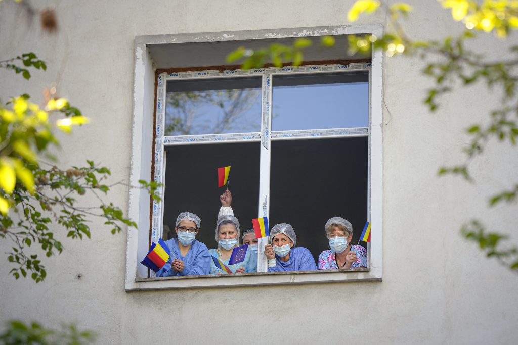 Medical staff of the Polizu maternity hospital hold European Union and Romanian flags while standing in a window to listen to a violinist playing to entertain them and the patients in Bucharest, Romania, Tuesday, April 28, 2020. Raluca Raducanu, a young violinist, played a mix of rock and classical pieces during an under one hour performance outside the hospital. 