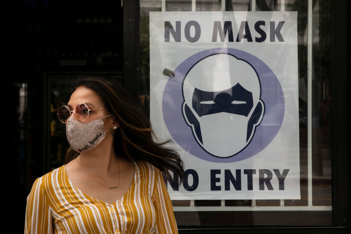 A woman walks out of a liquor store past a sign requesting its customers to wear a mask Tuesday, June 23, 2020, in Santa Monica, Calif. 
