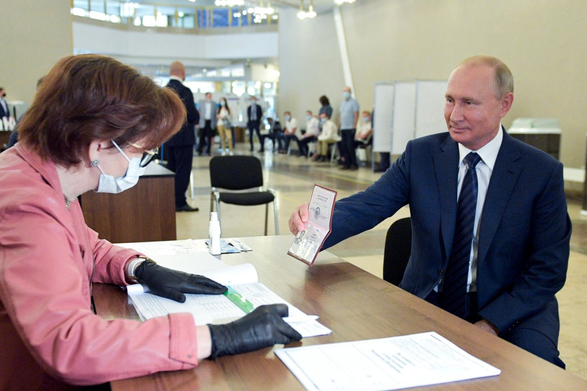 Russian President Vladimir Putin shows his passport to a member of an election commission as he arrives to take part in voting at a polling station in Moscow, Russia, Wednesday, July 1, 2020.