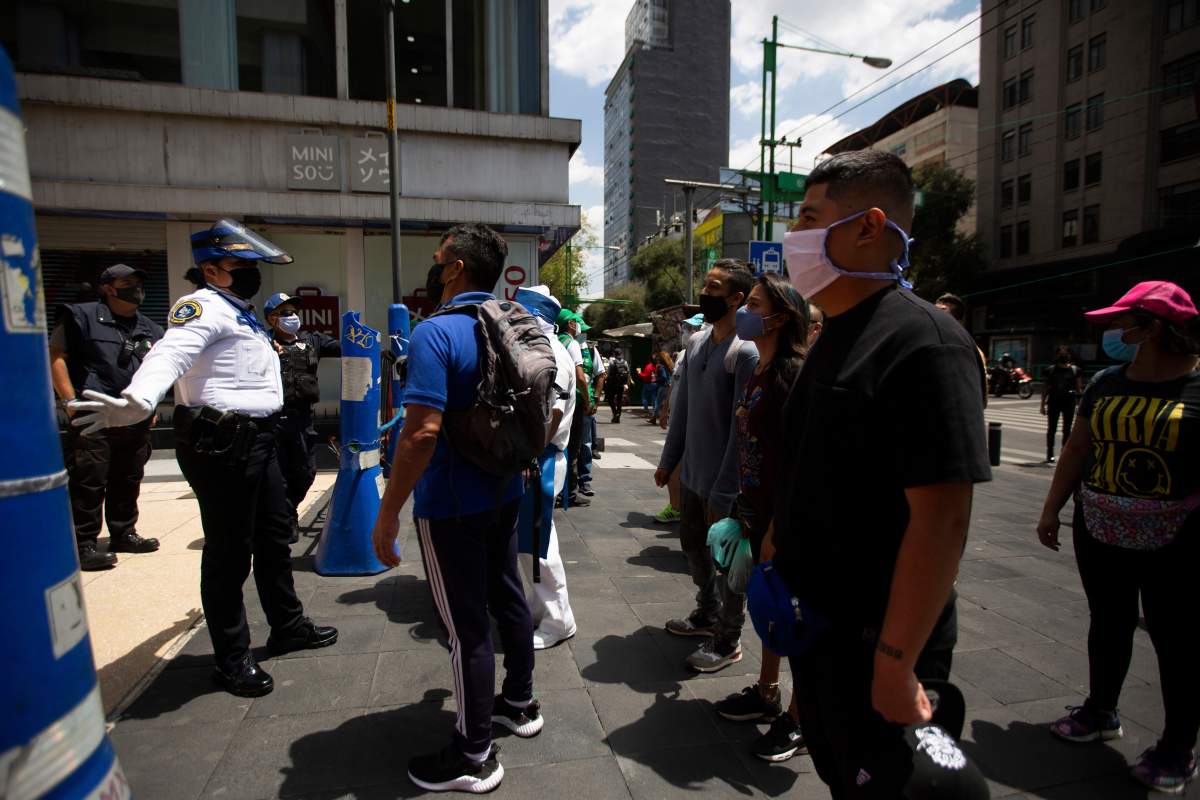 A Mexican police officer gives social-distancing and precautionary COVID-19 related guidelines to tourists in the historic center of Mexico City, Friday, July 3, 2020.