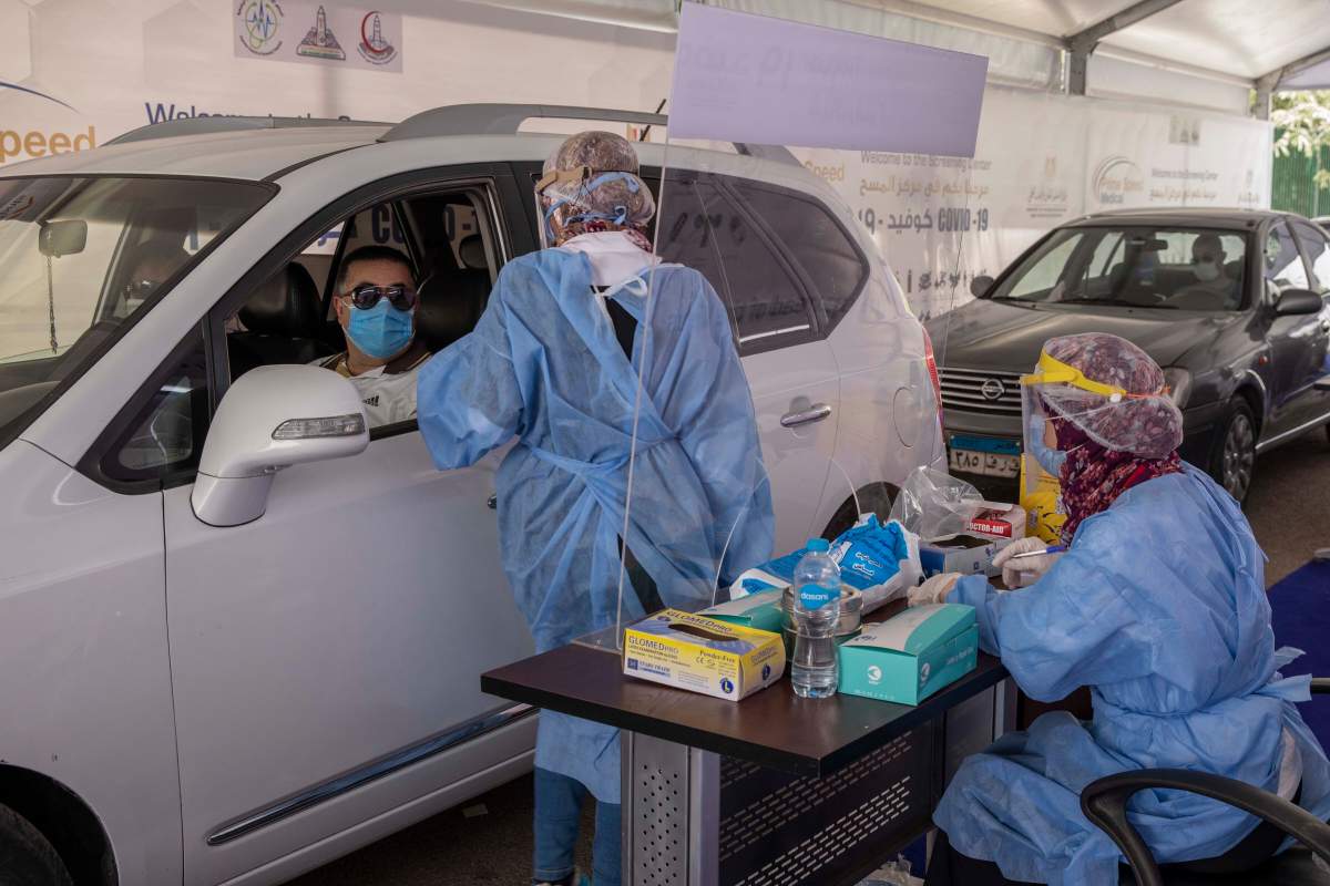 In this June 17, 2020 file photo, a health worker wearing protective gear prepares to take swab samples from people queuing in their cars to test for the coronavirus at a drive-through COVID-19 screening center at Ain Shams University in Cairo, Egypt.
