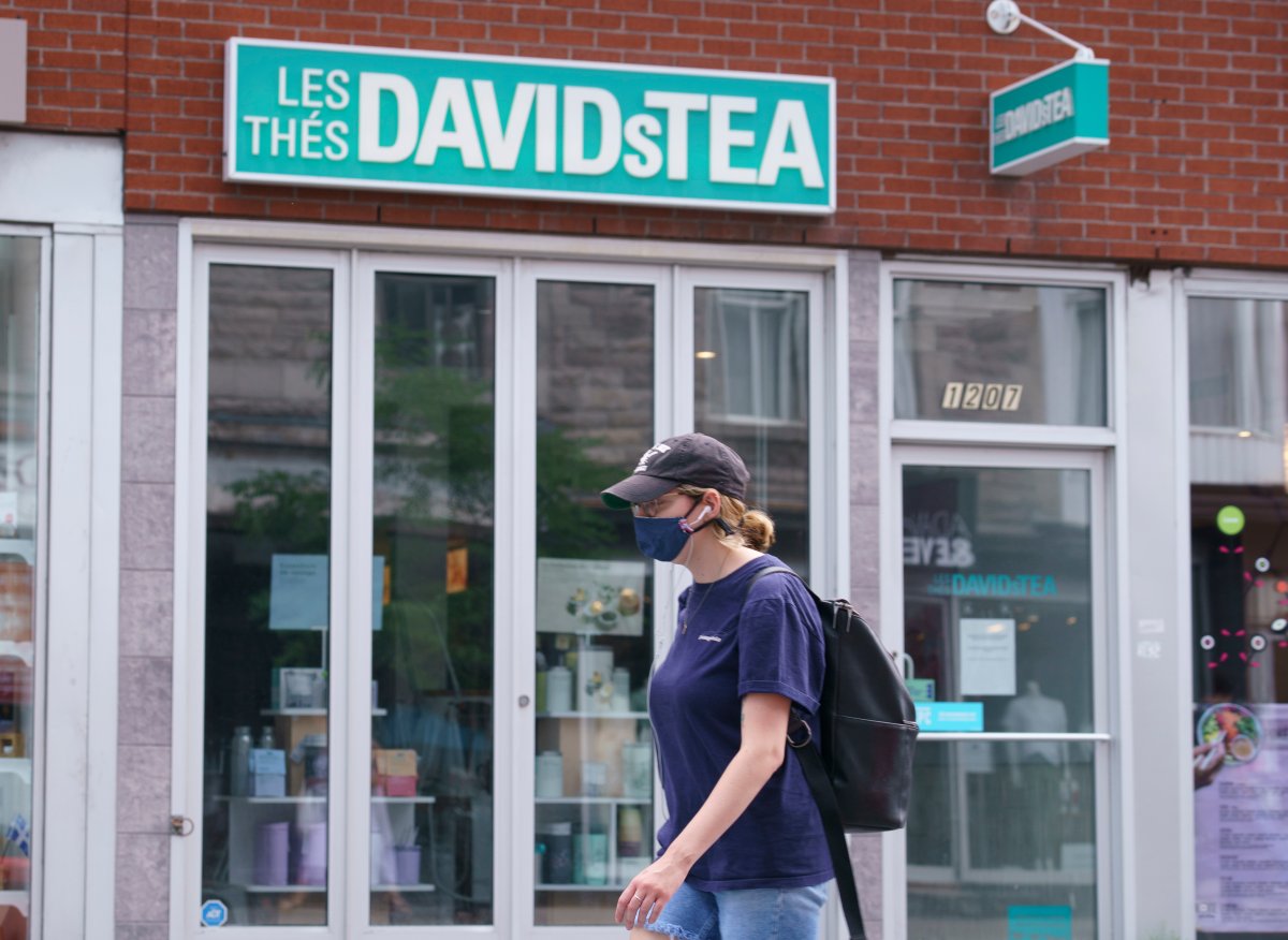 A woman wearing a protective mask walks past a closed DavidsTea store in Montreal on Wednesday, July 8, 2020.