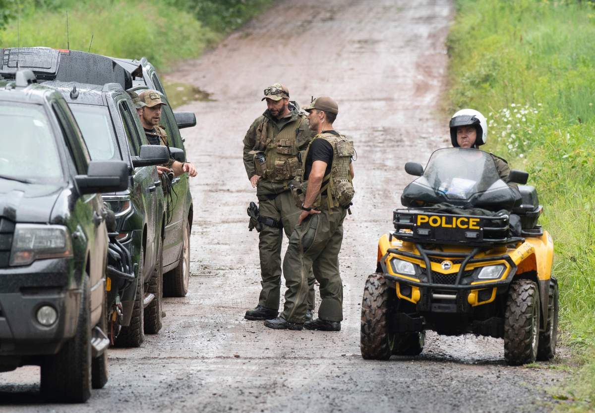 Police officer pause as they search a back road on Saturday, July 11, 2020 in Saint-Apollinaire, Quebec.  Quebec provincial police say two girls who were the subject of an Amber Alert have been found dead. 