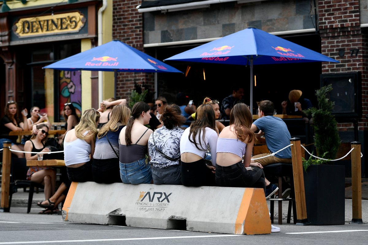 People sit on a cement block as they wait for a table at a bar's outdoor patio in the Byward Market in Ottawa, on Sunday, July 12, 2020, in the midst of the COVID-19 pandemic.
