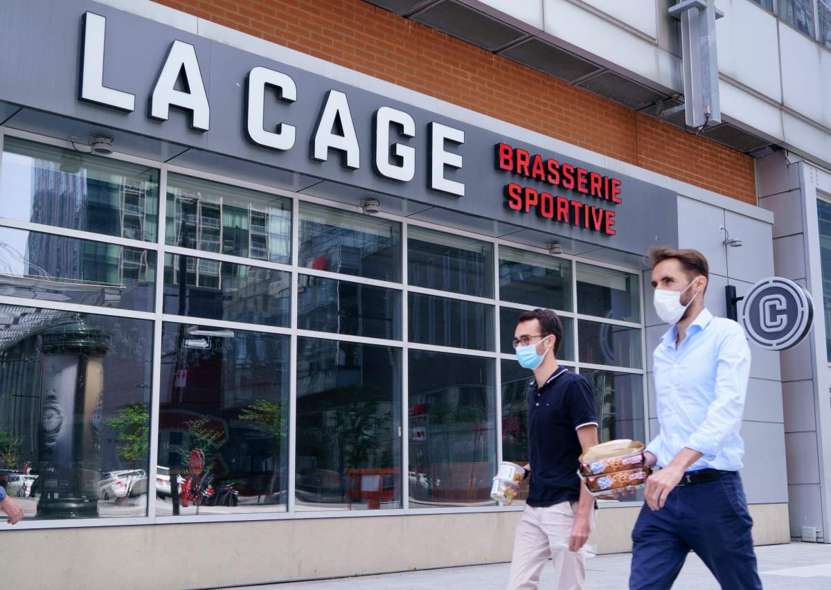 Two men walk past a La Cage Brasserie Sportive in Montreal, on Wednesday, July 22, 2020. The sports restaurant chain announced that will be cutting 30% of its staff.