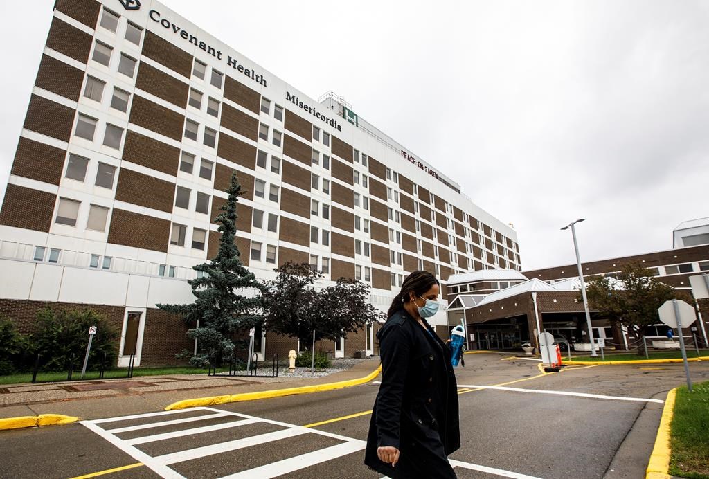 A person wearing a mask walks away from the Misericordia Community Hospital in Edmonton Alta, on Wednesday July 8, 2020. The hospital is no longer admitting patients due to a full outbreak of COVID-19. An outbreak at the Misericordia Community Hospital was first declared by Alberta's chief medical health officer two weeks ago, and restrictions were tightened as case numbers increased. THE CANADIAN PRESS/Jason Franson.